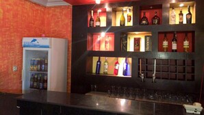 A bar area with shelves of liquor bottles, a refrigerator with beverages, and a counter with glasses. - Golden Bird Hotel & Suites (Lekki)