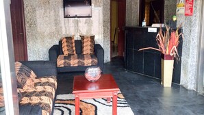 A lobby with a sofa, a coffee table, a reception desk, and a wall-mounted TV. - Golden Bird Hotel & Suites (Lekki)