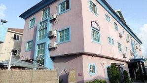 A multi-story building with a pink facade and blue trim. It features multiple windows, some with air conditioning units. - Golden Bird Hotel & Suites (Lekki)