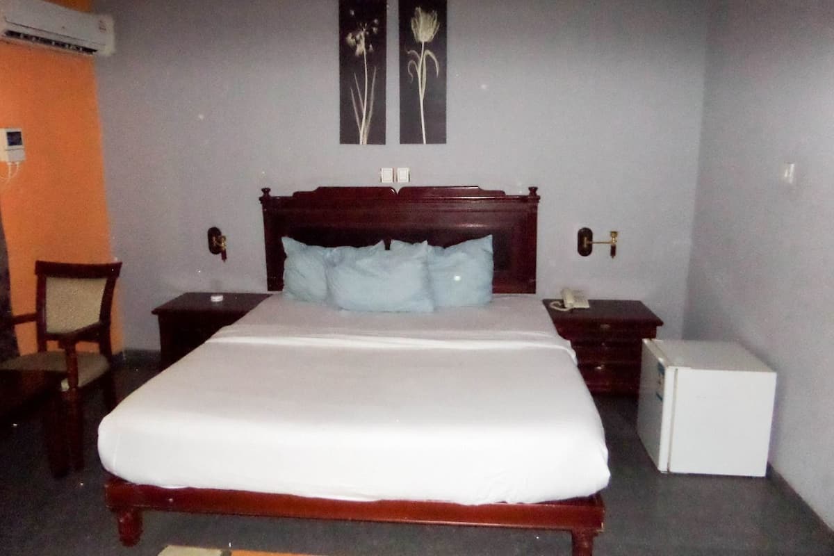 A bedroom with a wooden bed, two nightstands, a small white refrigerator, and a chair.