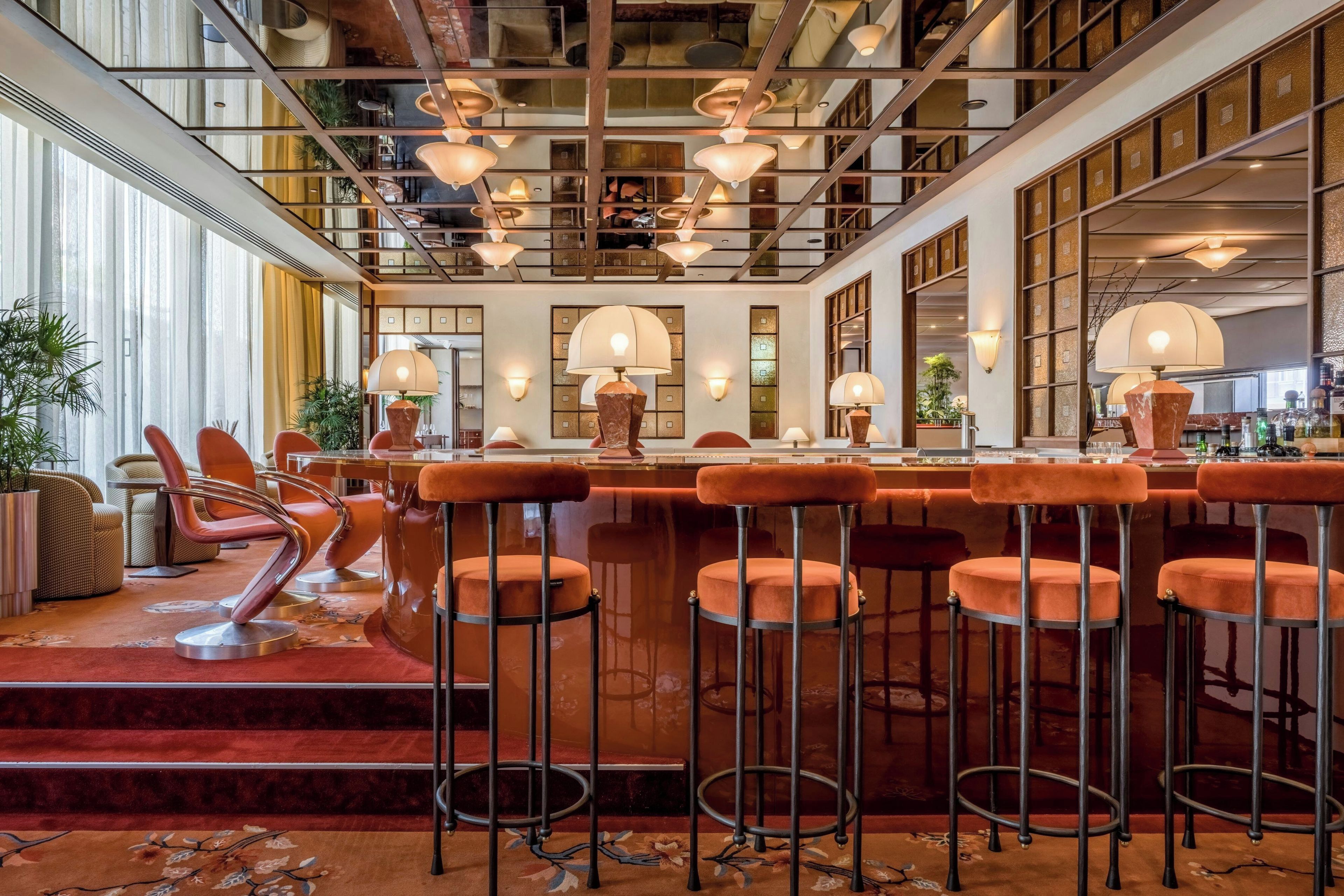 Eine Bar mit mehreren Hockern und einer Theke, ausgestattet mit Pendelleuchten und einem roten Teppich.