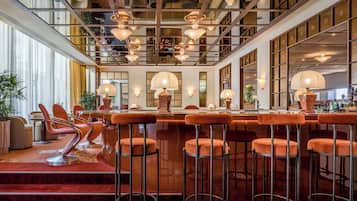 Eine Bar mit mehreren Hockern und einer Theke, ausgestattet mit Pendelleuchten und einem roten Teppich.