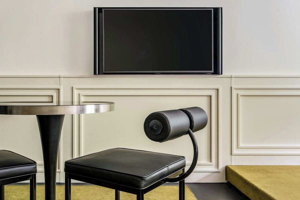 A modern room with a flat-screen TV mounted on the wall, a round table, a black chair, and a small sofa.
