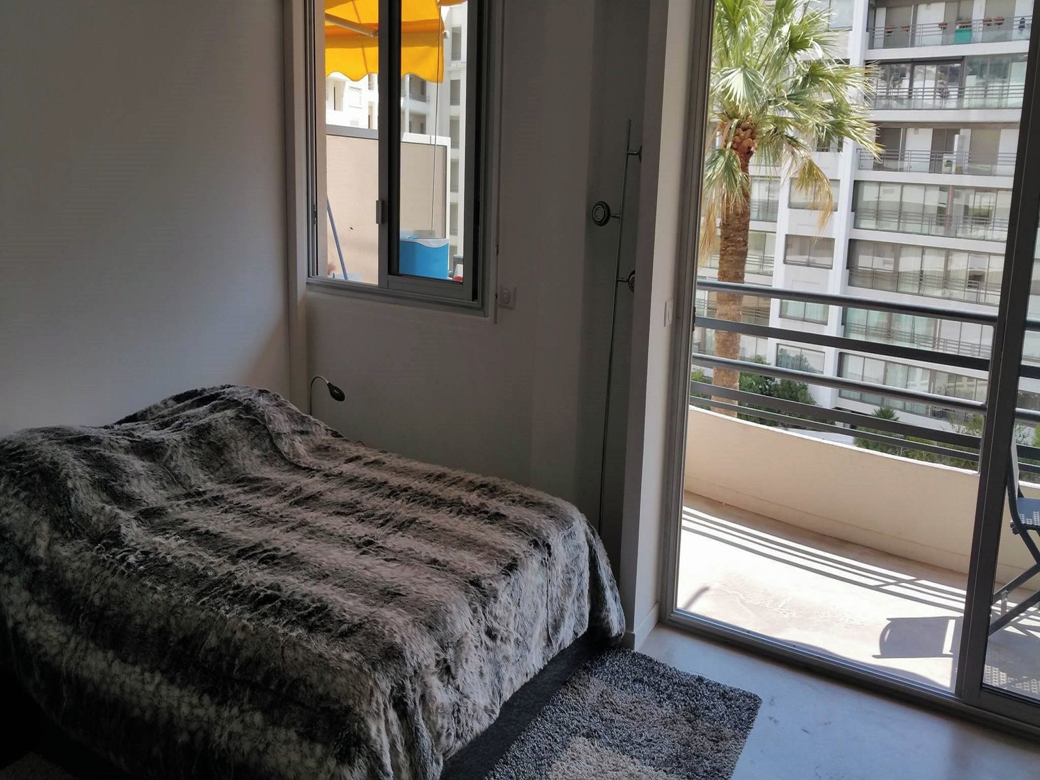 Une chambre à coucher avec un lit, une fenêtre et une vue sur un immeuble et un palmier.