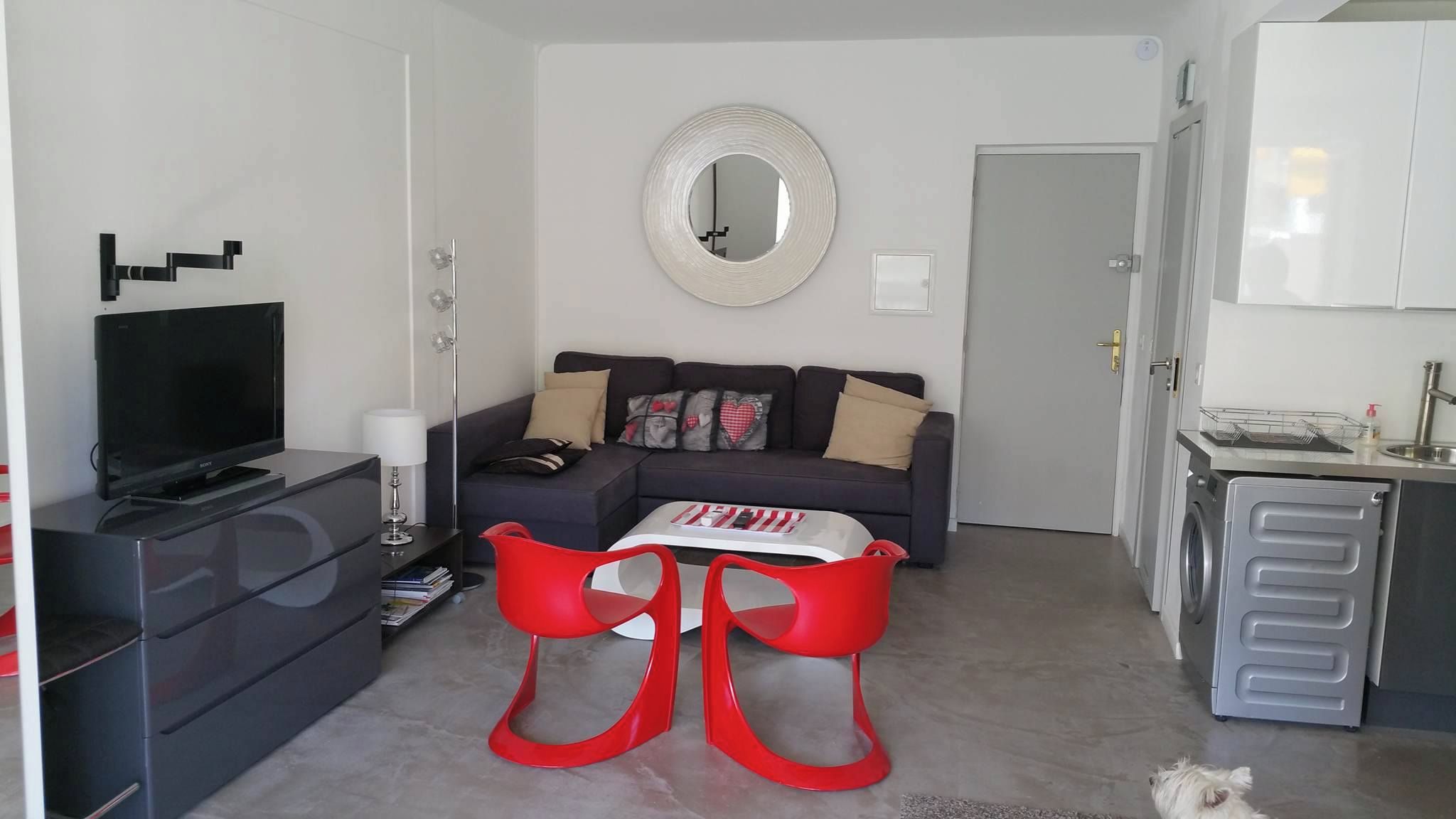 A living room with a sofa, a flat-screen TV, a coffee table, and a red chair.