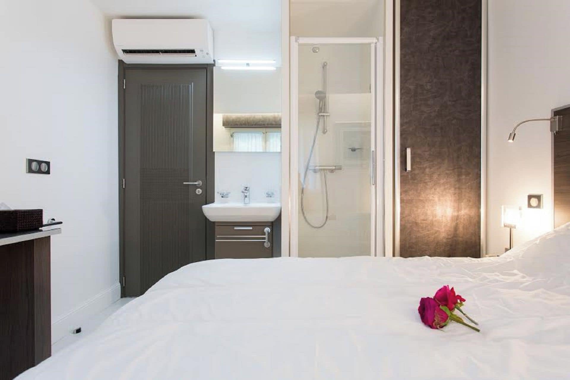 A hotel room with a bed, a shower, a sink, and a dark door.