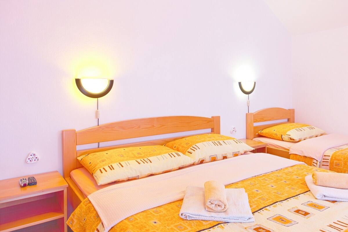 A hotel room with two beds, each with a wooden headboard, a bedside table, and a wall-mounted light fixture.