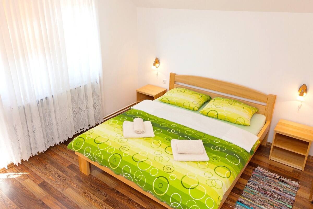 A neatly arranged bedroom with a bed, two bedside tables, a window with curtains, and a wooden floor.
