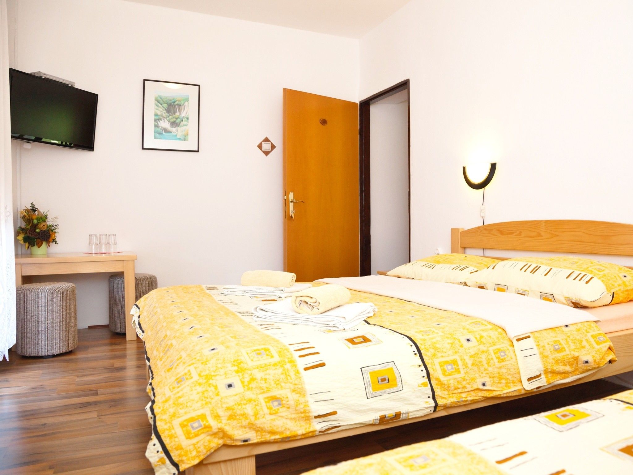 A hotel room with a bed, a desk, a TV, and a door.