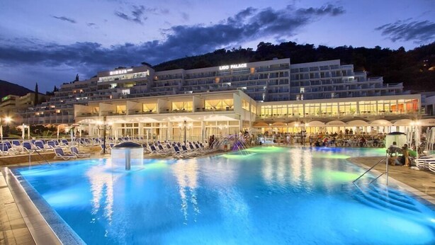 A hotel with a large pool area, multiple levels of balconies, and a well-lit exterior.