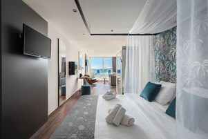 Quarto de hotel moderno com uma cama grande, televisão de tela plana, área de estar com vista e uma varanda.
