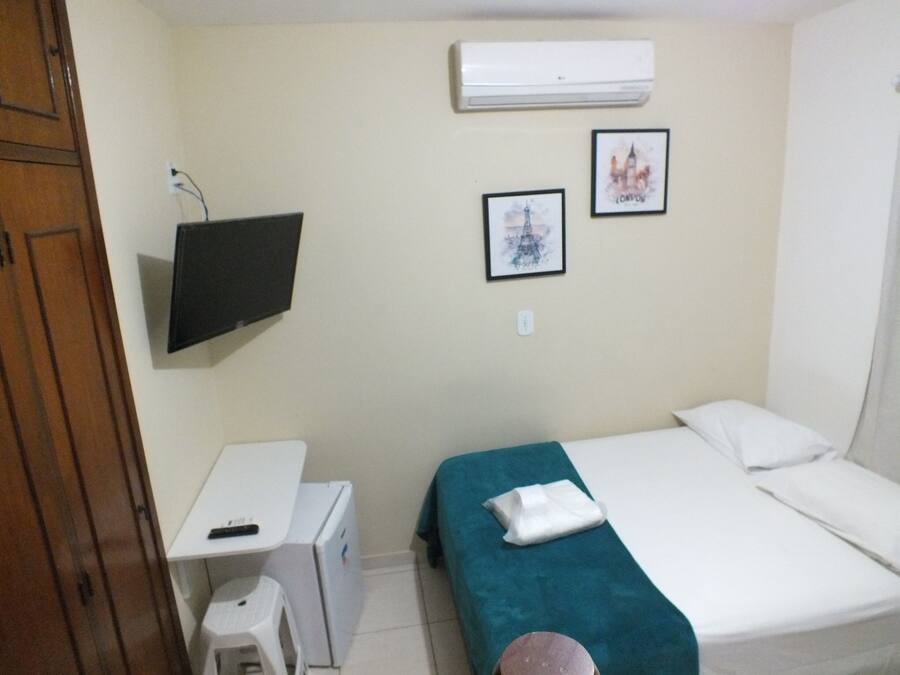 A small room with a bed, a desk, and a television mounted on the wall.