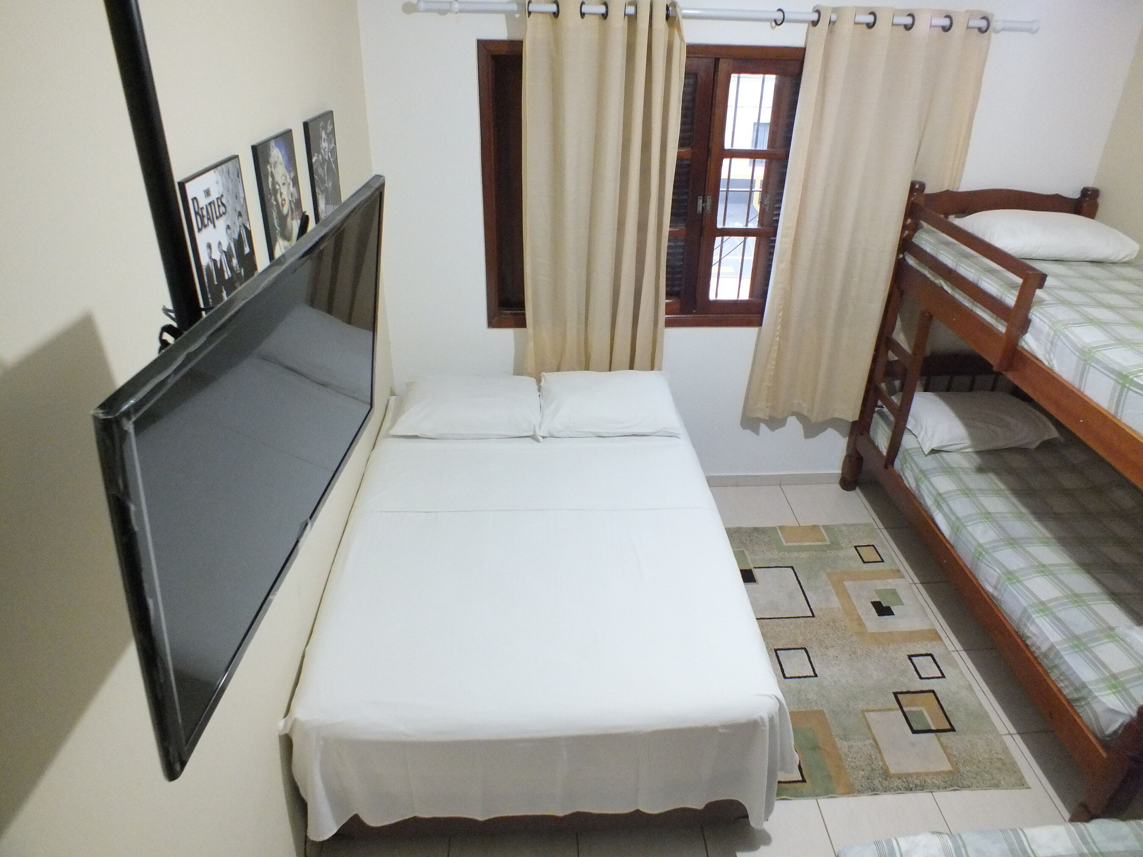 Un dormitorio con una cama individual, una litera, un televisor y una ventana con cortinas.