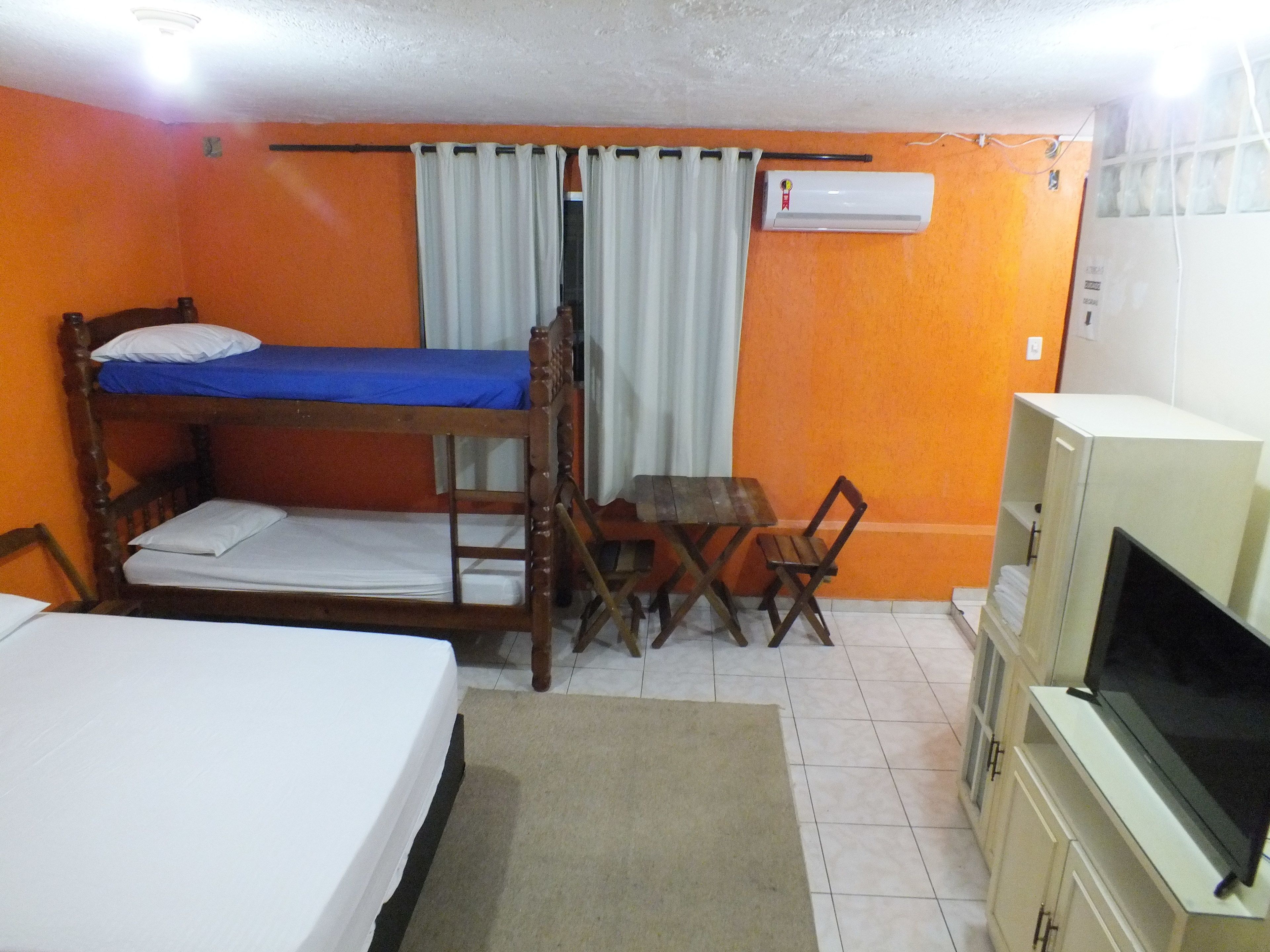 Una habitación con literas, una pequeña mesa con sillas, un televisor y un equipo de aire acondicionado.