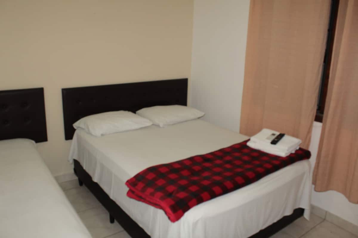 A single bed with a black headboard, white bedding, and a red and black checkered throw blanket.