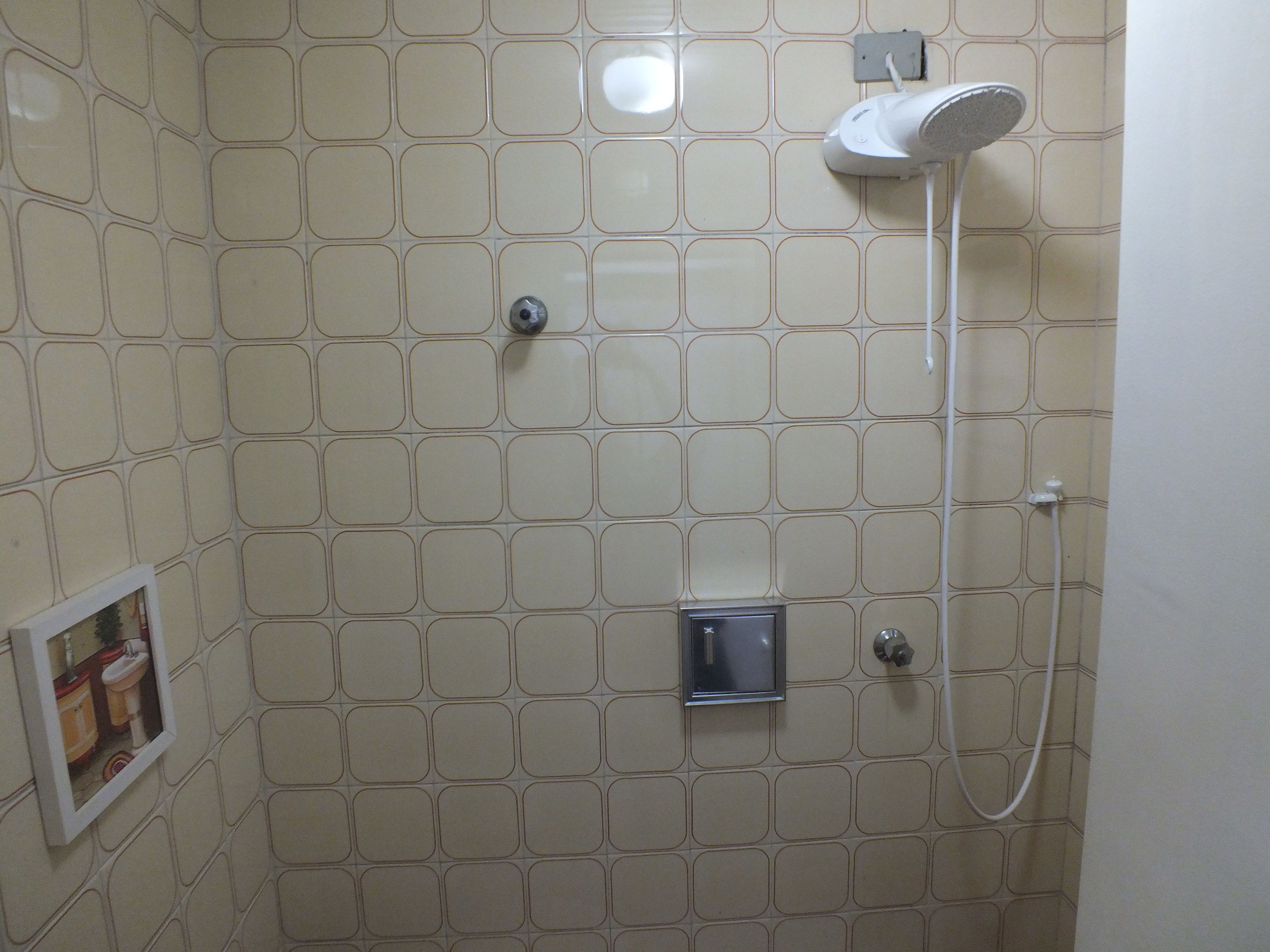 Une salle de bain avec un mur carrelé, une pomme de douche et un petit miroir.