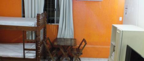 A room with a bunk bed, a dining table with chairs, an air conditioning unit, and a television.