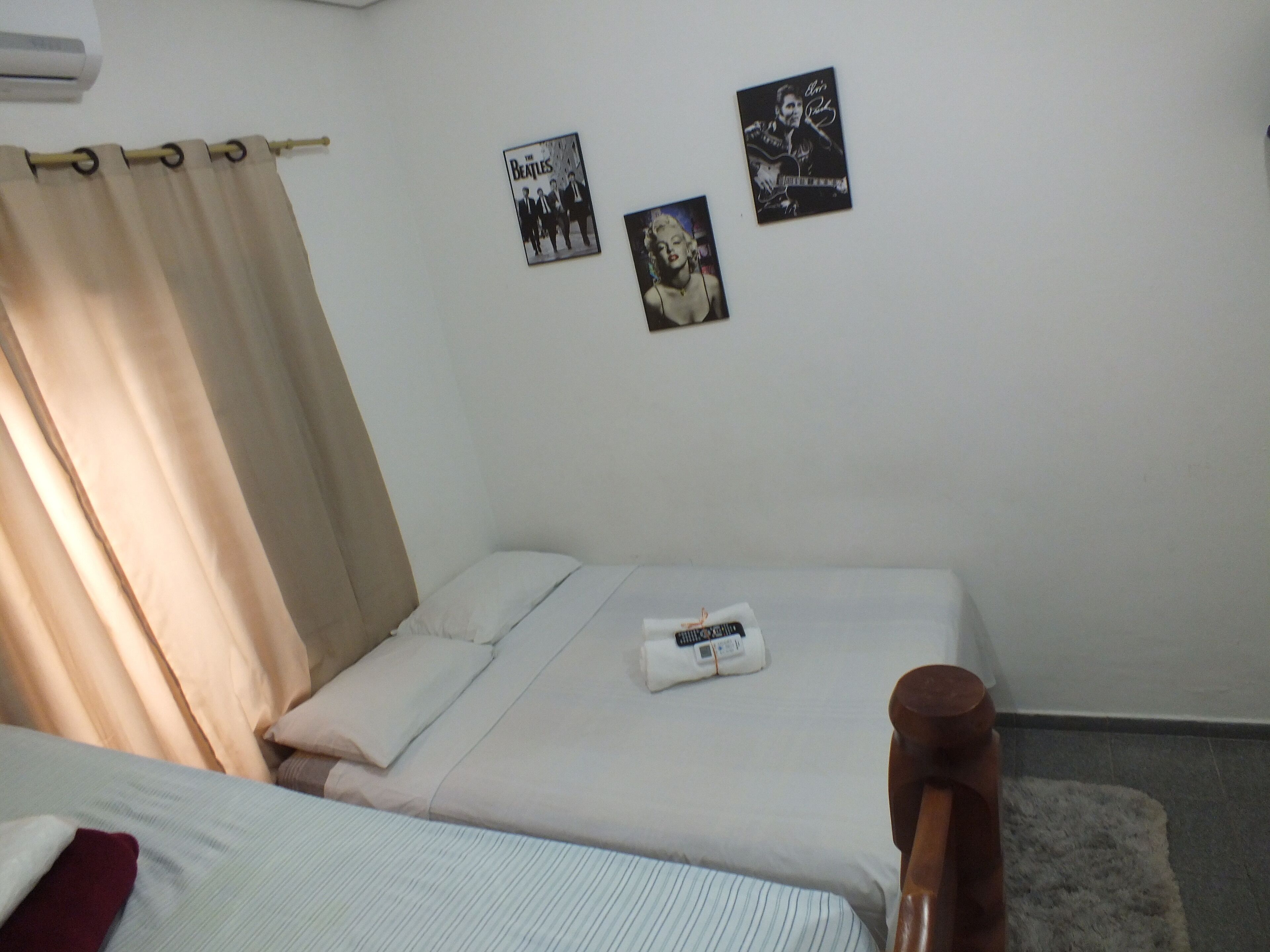 A bedroom with two beds, a wooden headboard, a white wall with posters, and a curtain.