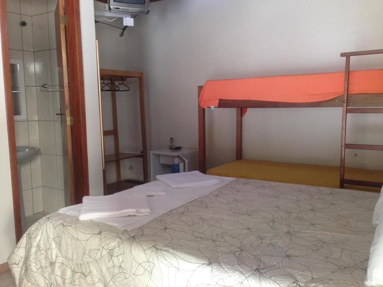 Une chambre avec un lit superposé, une table de chevet avec une lampe et une salle de bain avec une douche et un lavabo.