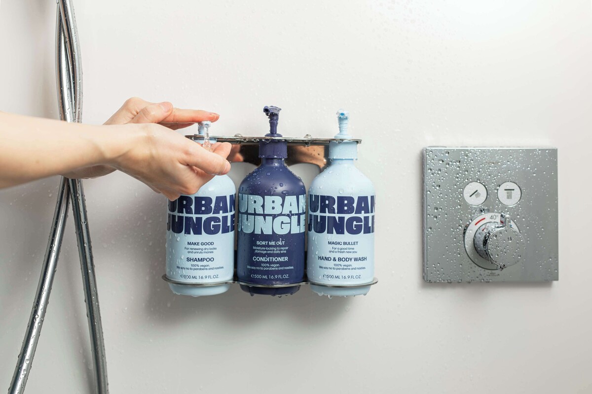 A hand adjusting a showerhead, three bottles of Urban Jungle products, and a water temperature control knob.