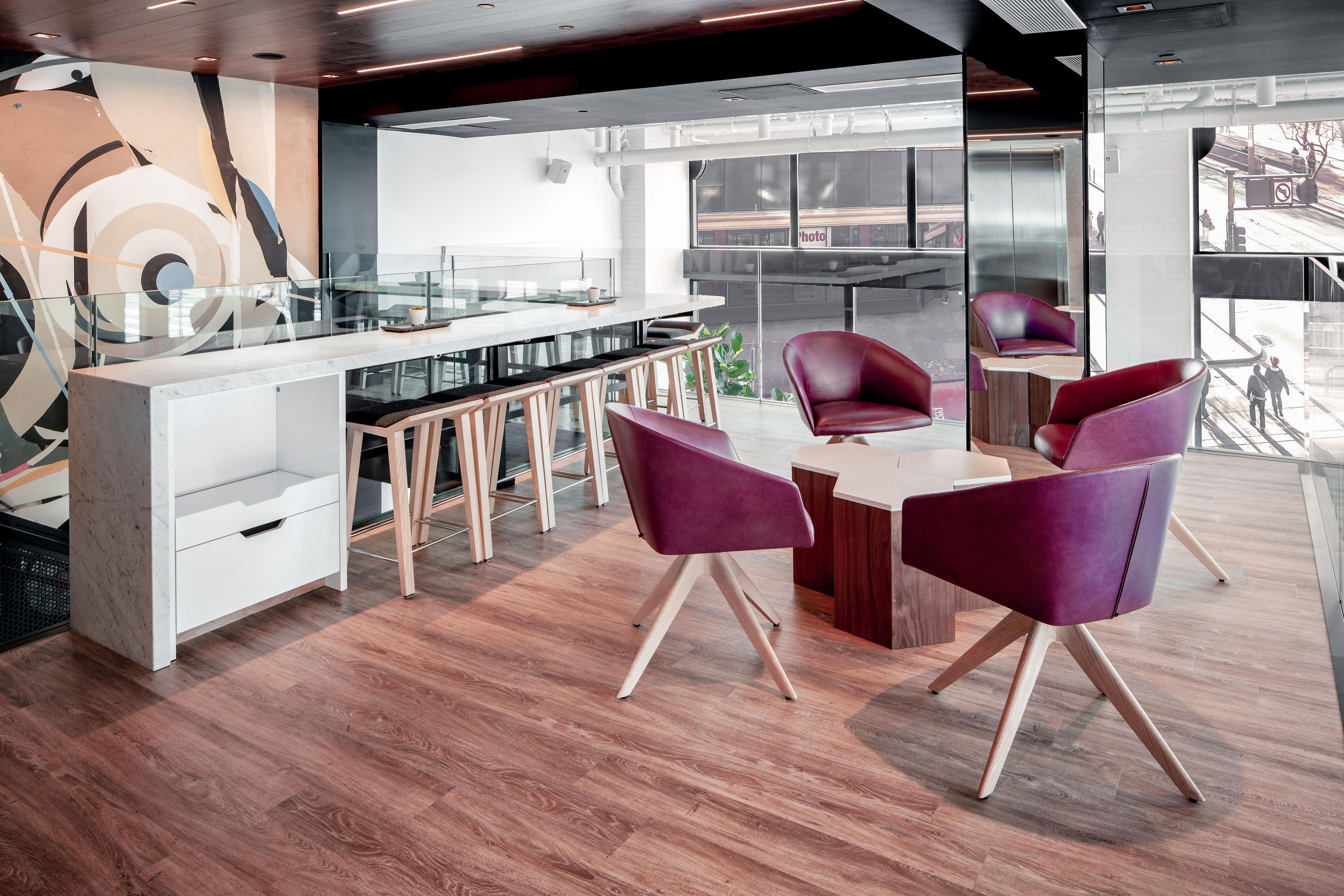 A modern office space with a glass partition, wooden flooring, and contemporary furniture.