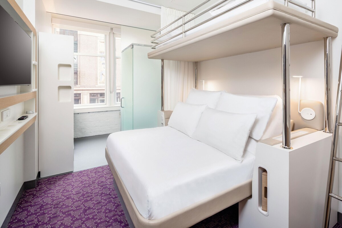 A hotel room with a bed, a television, a window, and a bathroom.