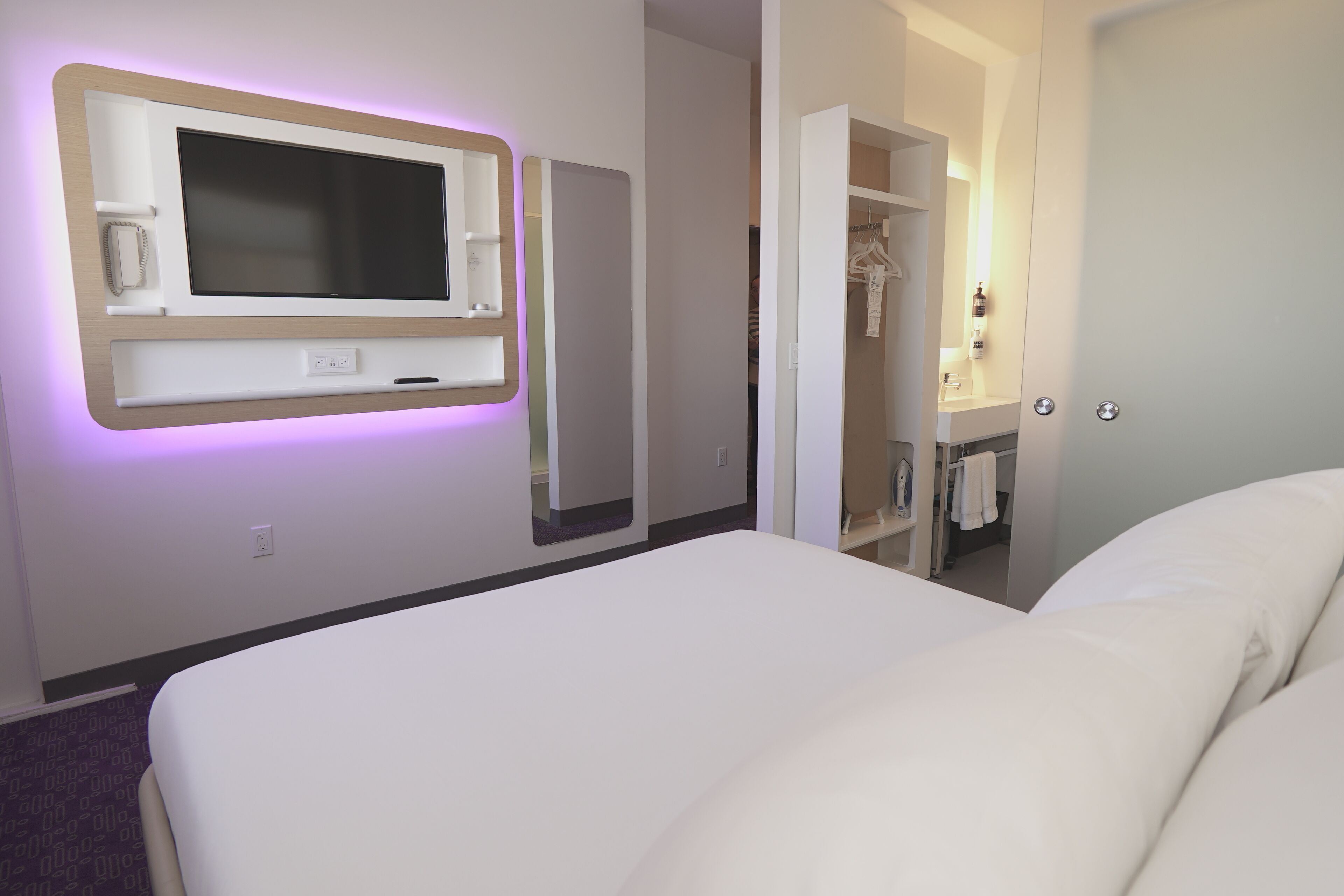 A hotel room with a large bed, a TV mounted on the wall, and a walk-in closet with a mirror.