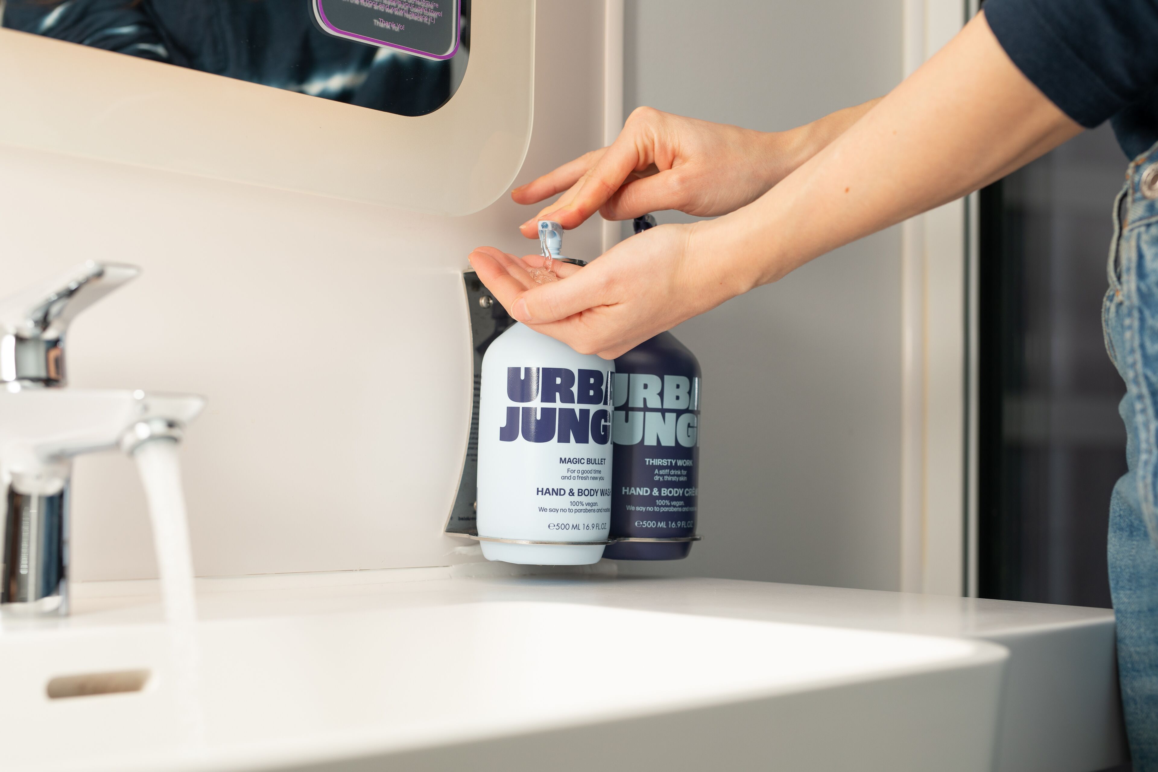 A hand dispensing a product from a dispenser labeled "URB JUNG" into a sink.