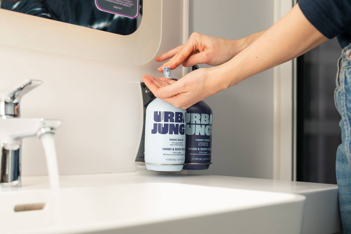 A hand dispensing a product from a dispenser labeled "URB JUNG" into a sink.