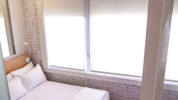Une chambre d’hôtel moderne avec un grand lit, une table de chevet, une fenêtre avec des stores et un mur en briques.