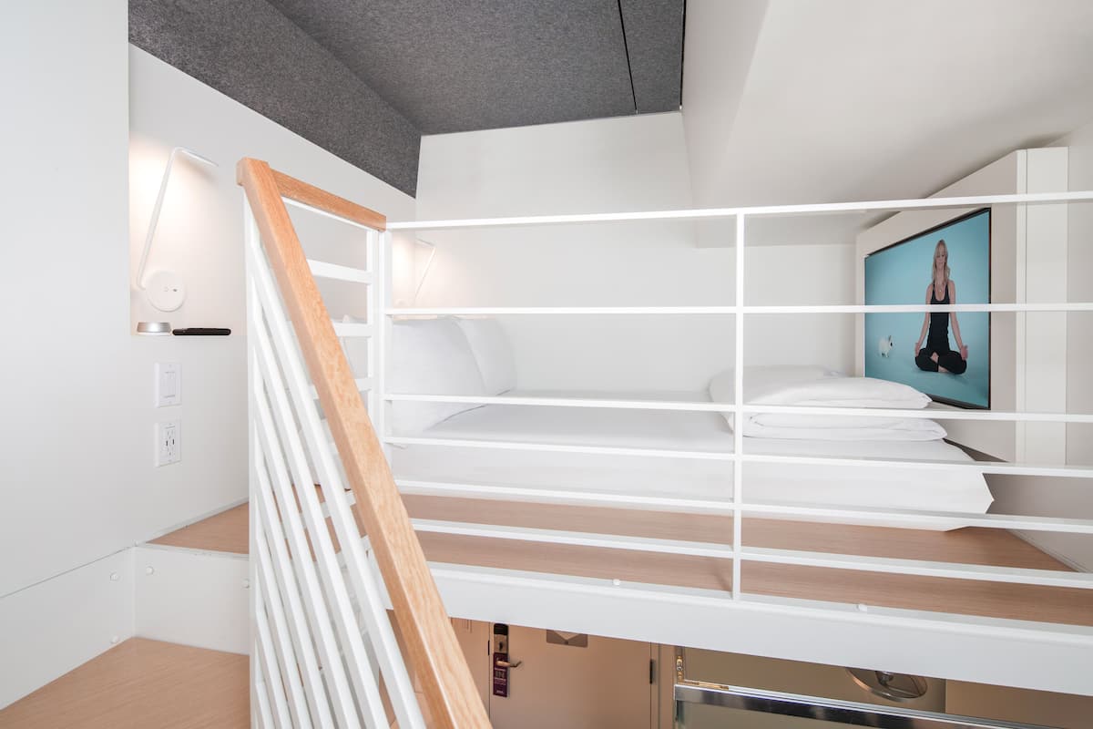 A modern, minimalist room with a bunk bed, a wooden staircase, and a wall-mounted TV displaying a yoga pose.