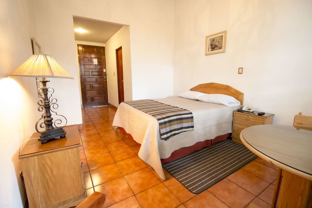 A bedroom with a bed, bedside table, lamp, and a small table with a chair.