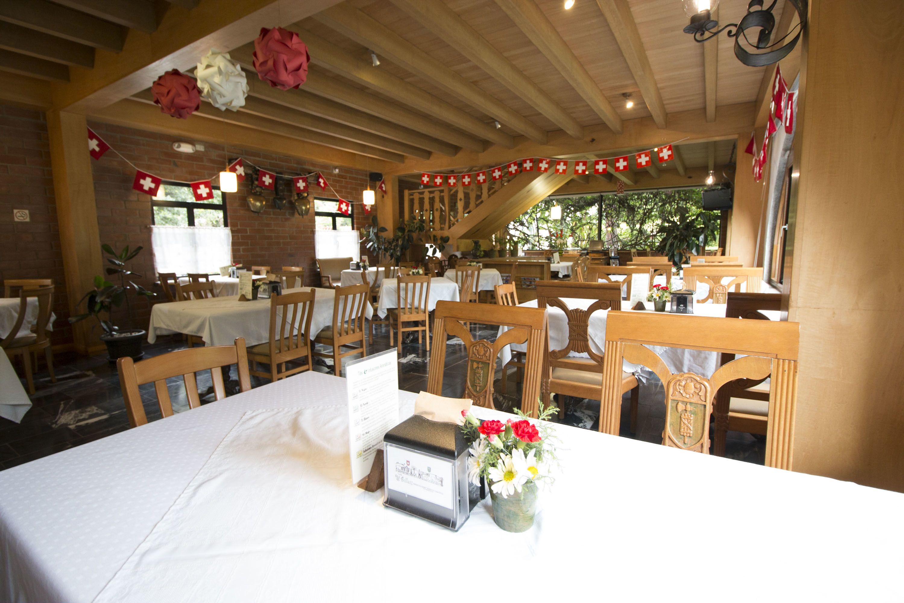 Un restaurante con mesas y sillas de madera, un atril para el menú y decoraciones con cruces rojas.