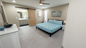 A bedroom with a bed, a nightstand, a dresser, a bathroom with a sink and mirror, and a sliding door to another room.