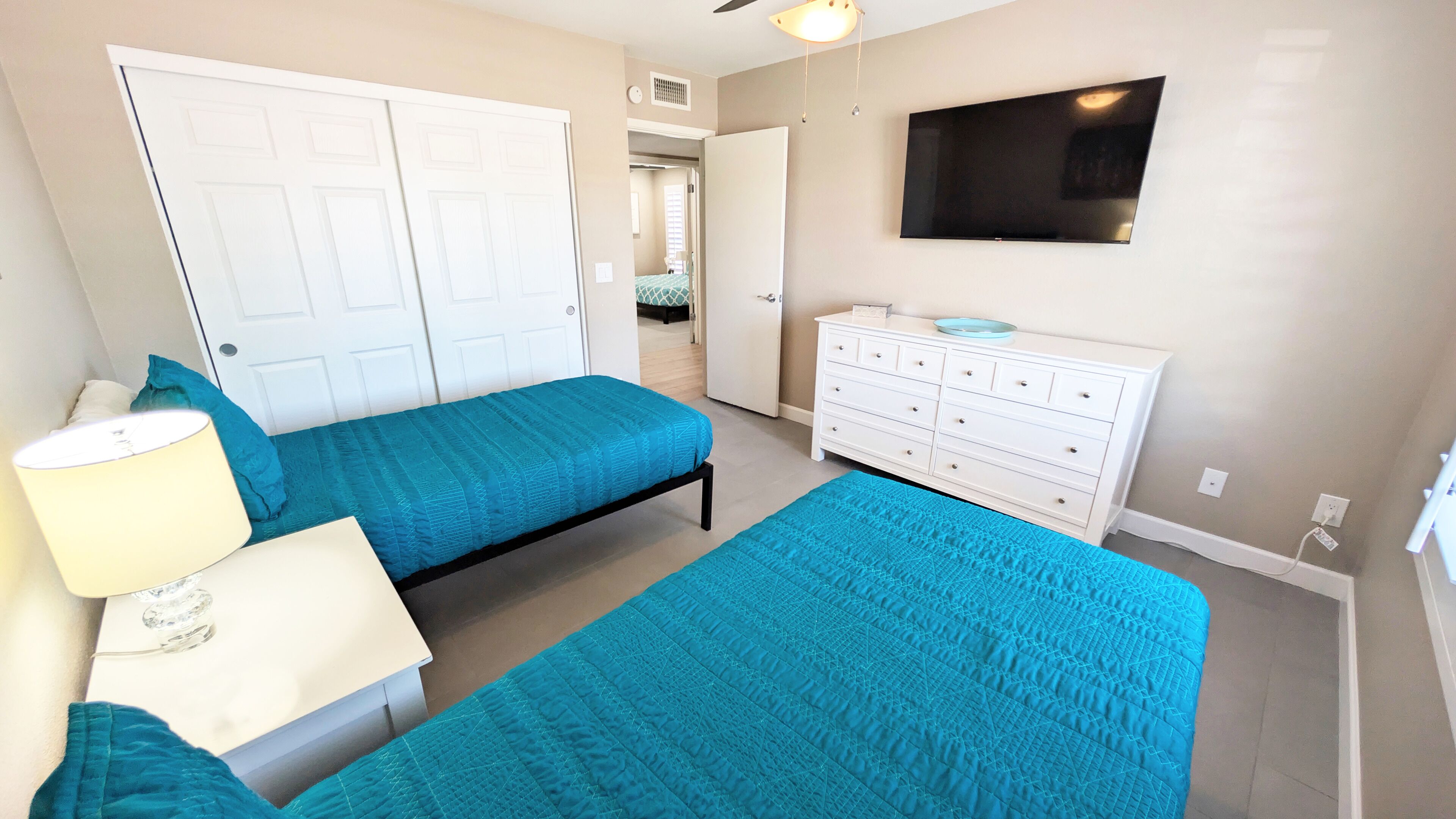 A bedroom with two beds, a dresser, a TV, and a lamp.