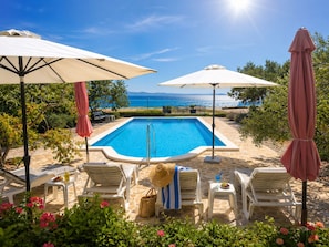 A pool with a clear view of the sea, surrounded by lounge chairs and umbrellas. - Seafront house with pool in Split,100m to the beach (Split)