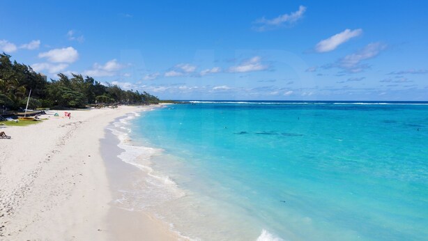 Una playa con aguas turquesas cristalinas, arena blanca y una línea de árboles al fondo.
