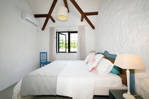 Une chambre à coucher avec un lit, une chaise, une lampe et une fenêtre avec des rideaux.