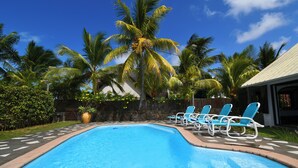 Una piscina con sillones de descanso, palmeras y un muro de piedra.