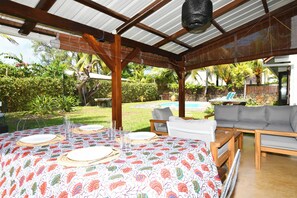 Une terrasse extérieure avec une table dressée pour le repas, un canapé et une piscine en arrière-plan.