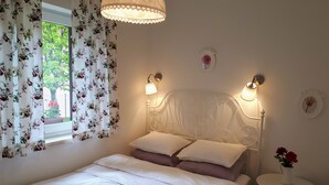 Una camera da letto con un letto, tende floreali, un comodino con un vaso e luci a parete.