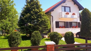 Una casa a due piani con un balcone, immersa nel verde e circondata da alberi.
