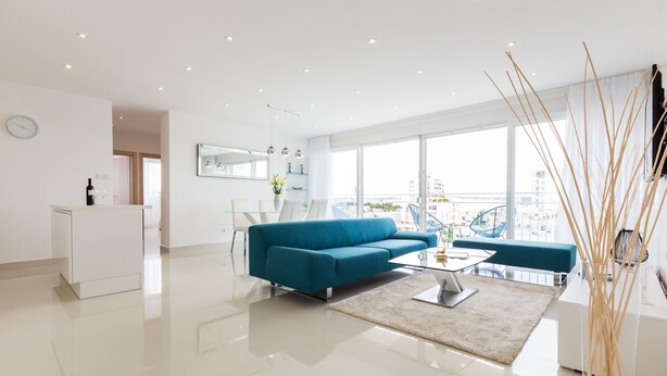 Een moderne woonkamer met een blauwe bank, een glazen salontafel en een stadszicht door grote ramen.
