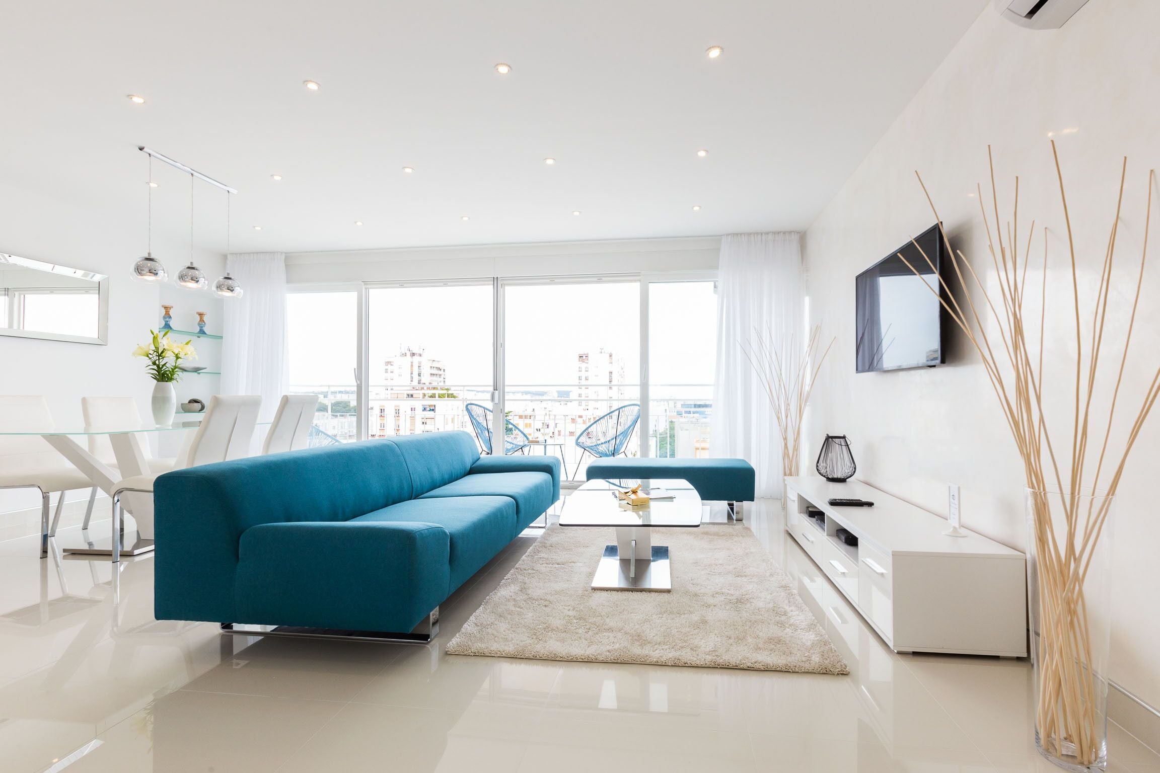 A modern living room with a blue sofa, a glass coffee table, and a flat-screen TV.