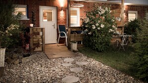 Una casa de ladrillo con una pérgola de madera, una puerta blanca y un jardín con un camino de grava.
