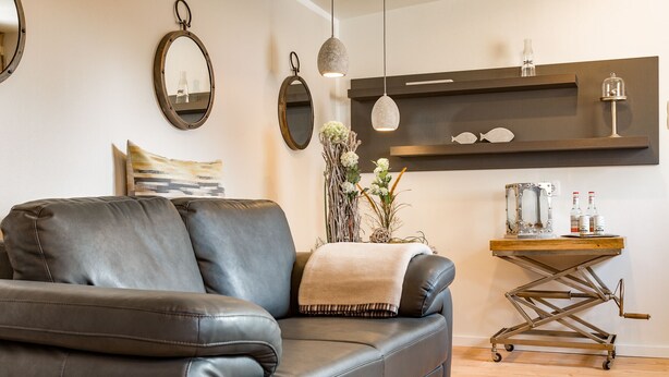 Una sala moderna con un sofá de cuero, una mesa de centro de madera y un jarrón decorativo con flores.