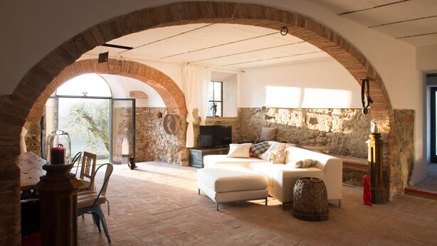 A spacious living area with a stone wall, a white sofa, and a television. - Tuscany romance. Rural charm between Montalcino and sea. Relax pur (Cinigiano)