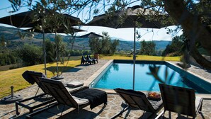 A swimming pool with lounge chairs and umbrellas, surrounded by a stone patio and a view of the countryside. - Tuscany romance. Rural charm between Montalcino and sea. Relax pur (Cinigiano)