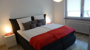 Un letto con biancheria bianca e una coperta rossa, affiancato da due comodini con lampade.