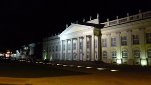 Un grande edificio illuminato con architettura classica, caratterizzato da colonne e un frontone, di notte.
